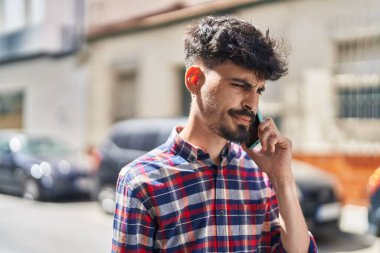 Young hispanic man talking on the smartphone at street