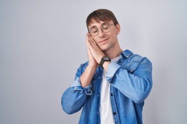 Kafkasyalı sarışın, gözlüklü, gözlüklü, yorgun, hayal kuran, elleriyle poz veren ve gözleri kapalı gülümseyen bir adam.. 