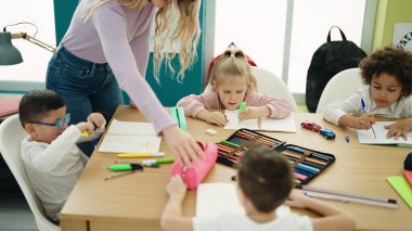 Sınıftaki masada ders alan kadın ve bir grup çocuk.