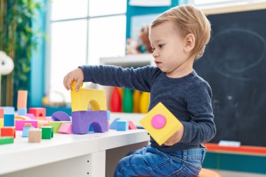 Anaokulundaki masada oturan sevimli sarışın çocuk geometri bloklarıyla oynuyor.
