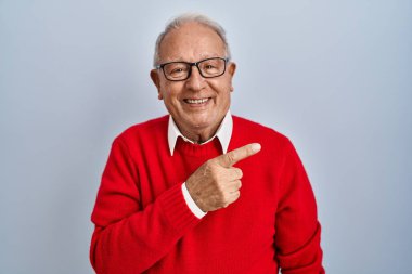 Gri saçlı yaşlı adam, izole edilmiş arka planda neşeli, yüzünde bir gülümseme, mutlu ve doğal bir ifadeyle elini ve parmağını kaldırmış bekliyor. 