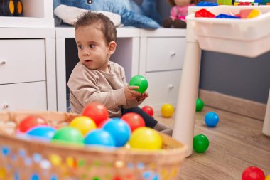 Anaokulunda yerde oturmuş toplarla oynayan sevimli İspanyol çocuk.