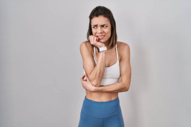 Tecrit edilmiş arka planda spor kıyafetleri giyen İspanyol kadın elleri ağızda tırnak yerken stresli ve gergin görünüyor. anksiyete. 