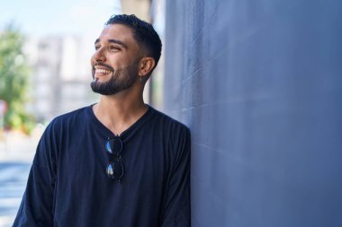 Genç Arap adam gülümsüyor. Kendinden emin. Caddenin kenarına bakıyor.