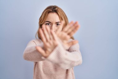 Hispanic woman standing over blue background rejection expression crossing arms and palms doing negative sign, angry face 