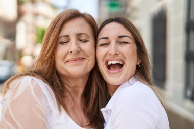 Anne ve kızı gülümsüyor, sokakta birbirlerine sarılıyorlar.