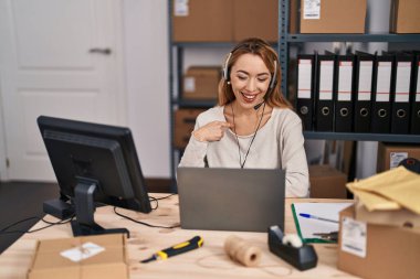 Küçük bir iş yerinde çalışan İspanyol bir kadın kulaklık takıyor ve gülümseyen mutlu ve gururlu birini işaret ediyor. 