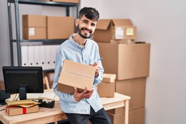 Latin kökenli genç bir iş adamı iş yerinde paket üzerine yazıyor.