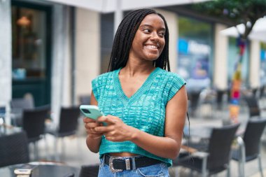 Afro-Amerikalı kadın sokakta akıllı telefon kullanarak kendine güveniyor.