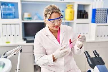 Young hispanic woman wearing scientist uniform analysing blood at laboratory