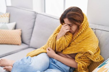 Young woman suffering headache covering with blanket at home
