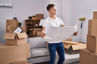 Young man architect smiling confident reading house plans at new home