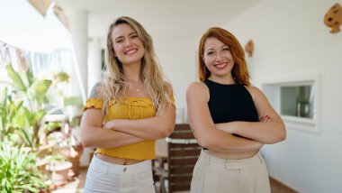 Two women smiling confident standing with arms crossed gesture at home terrace