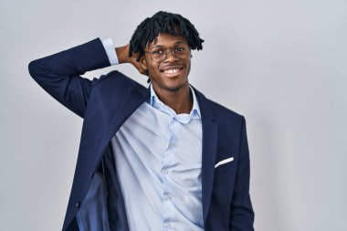 Beyaz arka planda iş ceketi giyen Afrikalı genç bir adam. Kendine güvenen, el hareketleriyle saçlarına dokunan, çekici ve modaya uygun poz veren. 