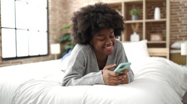 Afrika kökenli Amerikalı bir kadın yatakta akıllı telefon kullanıyor.