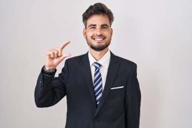 Dövmeli, takım elbiseli, kravatlı, gülümseyen, kendine güvenen, el hareketleriyle hareket eden parmakları küçük gösteren ve kameraya bakan İspanyol bir genç. ölçüm kavramı. 