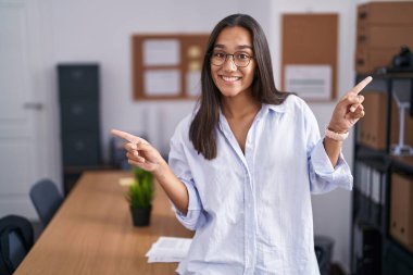 Ofisteki genç İspanyol kadın farklı yönleri işaret ederek kendine güvenerek gülümsüyor. reklam için kopyalama alanı 