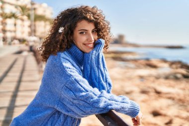 Genç İspanyol kadın gülümsüyor. Kendine güveniyor. Deniz kenarındaki balyalara yaslanıyor.