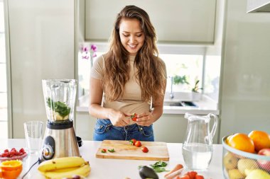 Genç ve güzel İspanyol kadın mutfakta çilek doğrayan blender ile sebze suyu hazırlıyor.