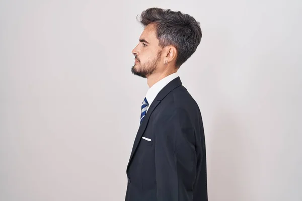 Young hispanic man with tattoos wearing business suit and tie looking to side, relax profile pose with natural face and confident smile.