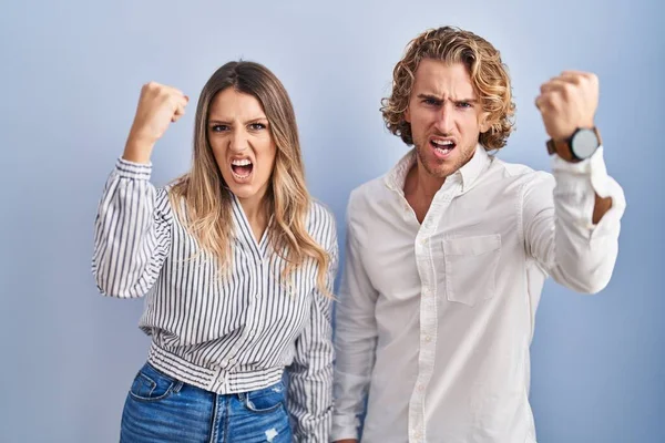 Young Couple Standing Blue Background Angry Mad Raising Fist Frustrated — Stock Photo, Image