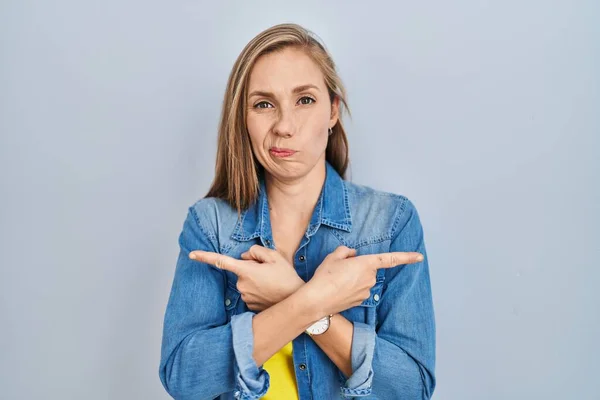 Mladá Blondýnka Stojící Nad Modrým Pozadím Ukazující Prsty Obě Strany — Stock fotografie