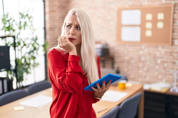オフィスで働く白人女性は 口の爪をかむ上で手で強調し 緊張しているように見えるタブレットで働いています 不安の問題 — ストック写真