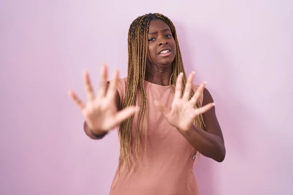 身穿辫子的非裔美国妇女站在粉色背景上 害怕而且害怕 恐惧的表情 用手停止手势 震惊地大叫 恐慌概念 — 图库照片