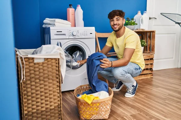 洗濯室で自信を持って洗濯服を笑っている若いアラブ人男性 — ストック写真