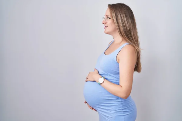 若いです妊娠中の女性立ちます上の白い背景を見ます側 リラックスプロファイルポーズとともに自然顔と自信満面の笑顔 — ストック写真