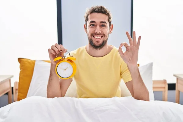 Ισπανόφωνος Άνθρωπος Γενειάδα Κρατώντας Ξυπνητήρι Στο Κρεβάτι Κάνει Υπογράψει Δάχτυλα — Φωτογραφία Αρχείου