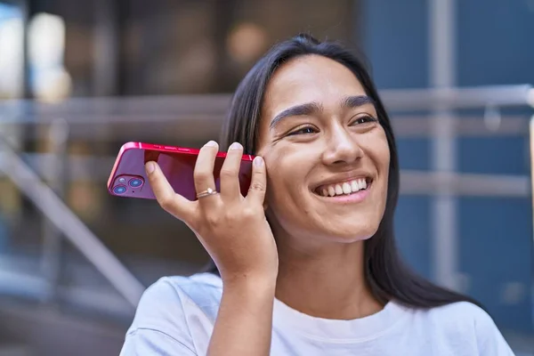 若い美しいヒスパニック系の女性は通りでスマートフォンによって自信を持ってリスニング音声メッセージを笑います — ストック写真