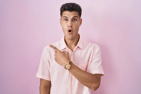 Young Hispanic Man Standing Pink Background Surprised Pointing Finger Side — 스톡 사진