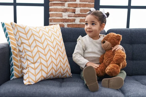 Adorable Hispanic Girl Hugging Teddy Bear Sitting Sofa Home — Stockfoto