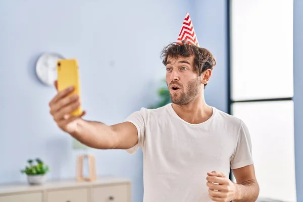 Joven Hispano Usando Sombrero Cumpleaños Haciendo Videollamada Con Smartphone Asustado —  Fotos de Stock
