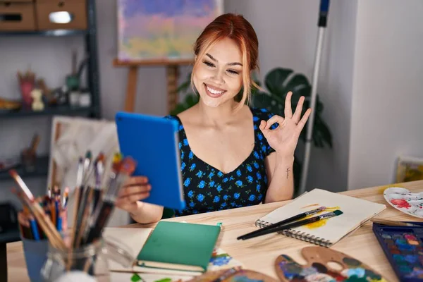 若いですCaucasian女性座っていますでアートスタジオ行いますビデオコールとともにタブレットDoing Signとともに指 笑顔優しいジェスチャー優れたシンボル — ストック写真