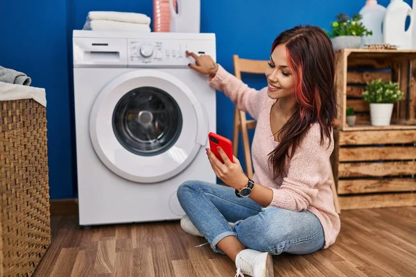 年轻的高加索女人在洗衣房用智能手机打开洗衣机 — 图库照片