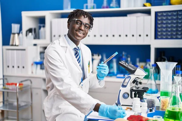 African american man scientist writing report holding test tube at laboratory