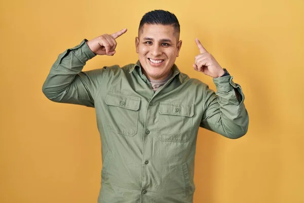 Jovem Hispânico Sobre Fundo Amarelo Sorrindo Apontando Para Cabeça Com — Fotografia de Stock