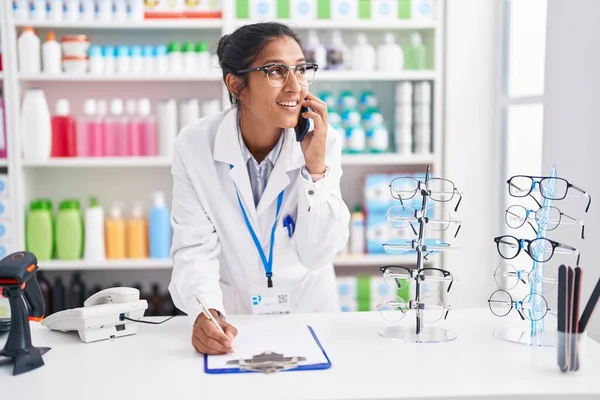 Young Beautiful Hispanic Woman Pharmacist Talking Smartphone Writing Document Pharmacy — Stockfoto