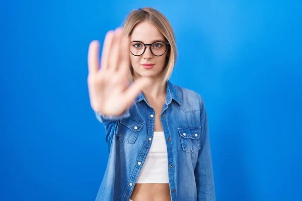 年轻的高加索女人站在蓝色的背景上 用手掌停止歌唱 用消极而严肃的手势警告人 — 图库照片
