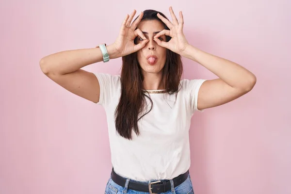 Young Brunette Woman Standing Pink Background Doing Gesture Binoculars Sticking — Stok fotoğraf