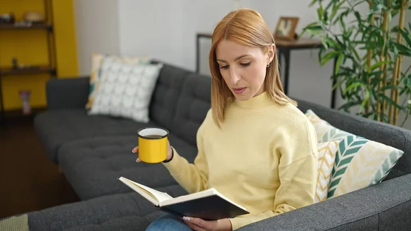 Genç Sarışın Kadın Kitap Okuyor Evdeki Kanepede Oturup Kahve Içiyor — Stok fotoğraf