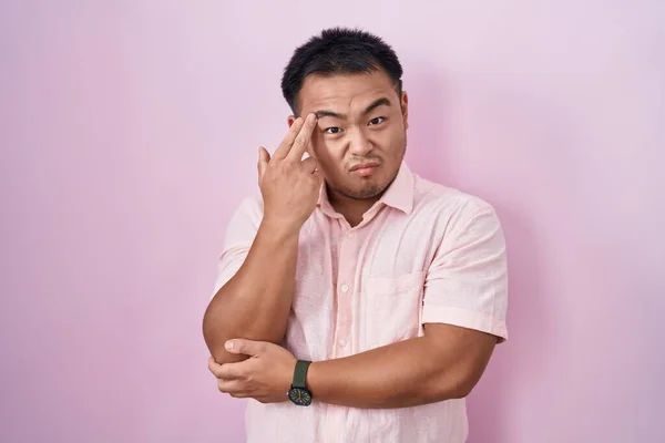 ピンクの背景に立っている中国の若者は銃のように頭に手と指を指して自殺した — ストック写真