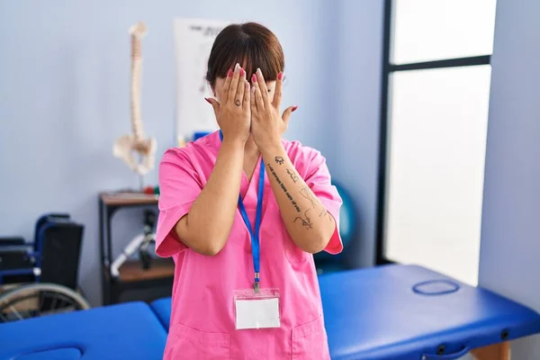 泣きながら手で顔を覆う悲しい表情でリハビリクリニックで働く若いブルネットの女性 うつ病の概念 — ストック写真