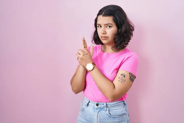 ピンクの背景に立っている若いヒスパニック系の女性は 手のジェスチャーで象徴的な銃を保持します シューティングゲームをプレイ 怒っている顔 — ストック写真