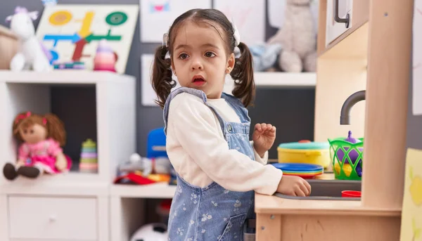 可爱的惊恐女孩站在幼儿园里玩着游戏厨房 — 图库照片