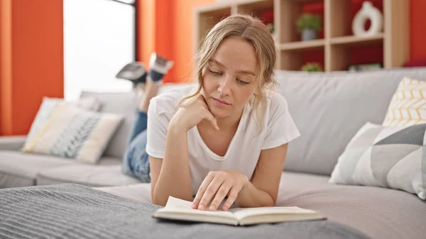 Young Blonde Woman Reading Book Lying Sofa Home — Stock fotografie