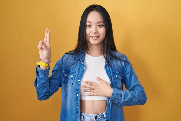 Молодая Азиатка Стоящая Жёлтом Фоне Улыбаясь Ругаясь Рукой Груди Пальцах — стоковое фото