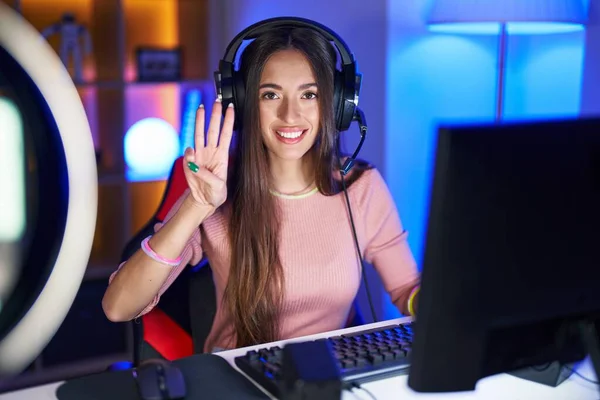 stock image Young hispanic woman playing video games showing and pointing up with fingers number three while smiling confident and happy. 